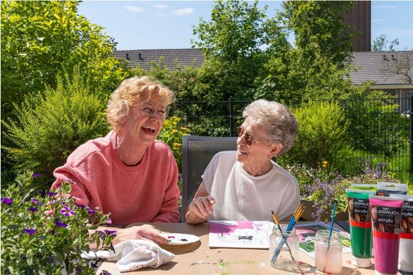 Een vrijwilliger en een oudere dame lachen tijdens het schilderen 