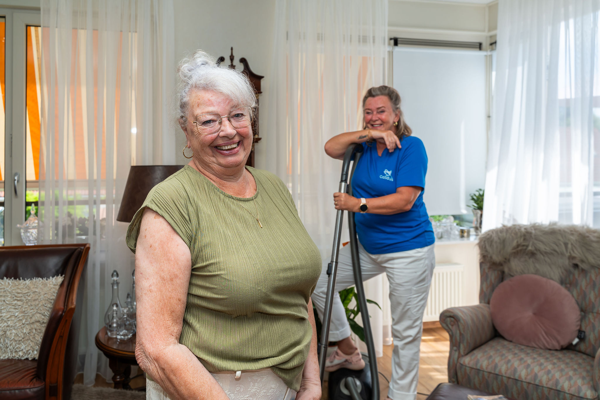 Vrouw kijkt naar camera en vrouw op achtergrond met stofzuiger