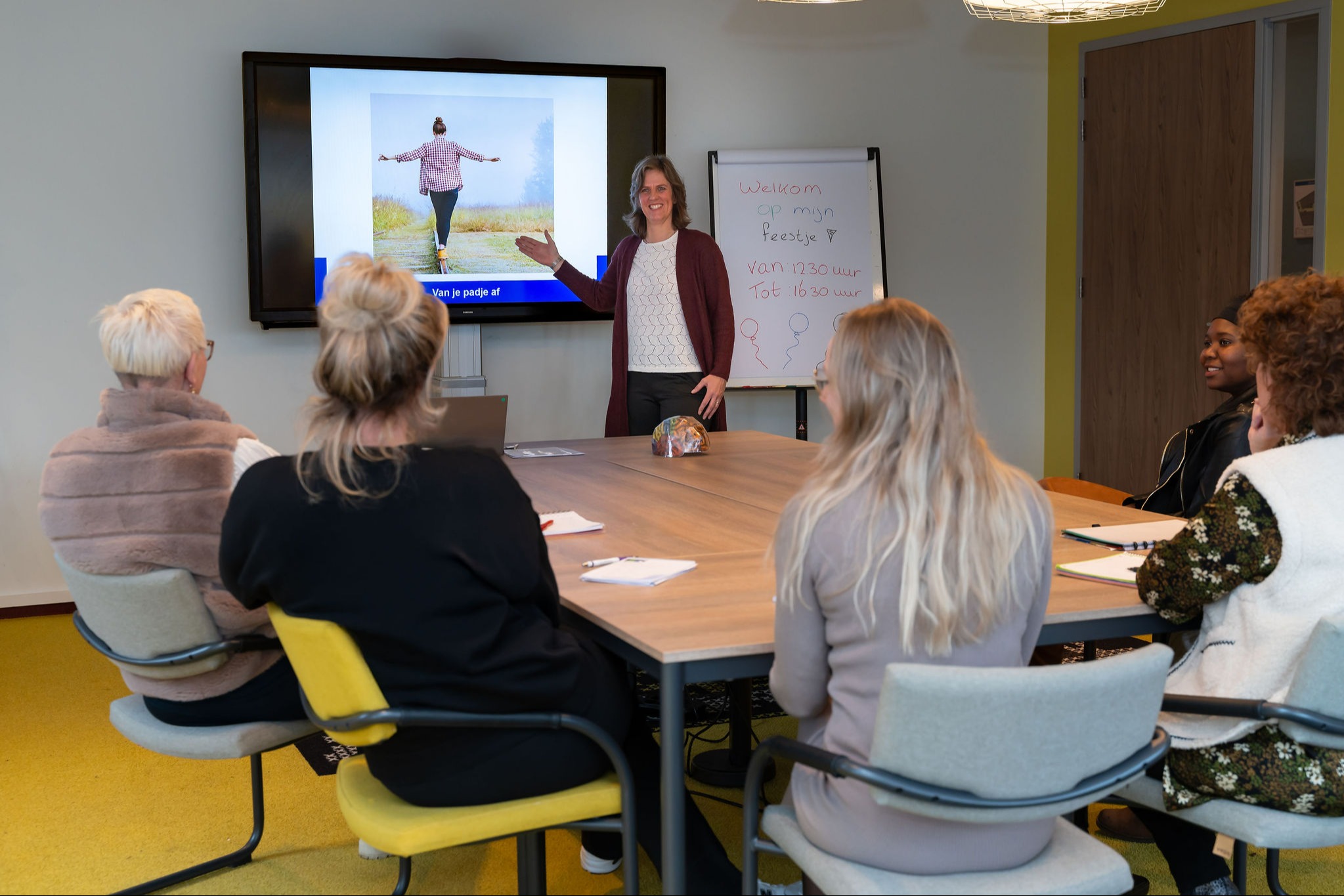 Groep mensen zitten aan tafel en luisteren naar een trainer