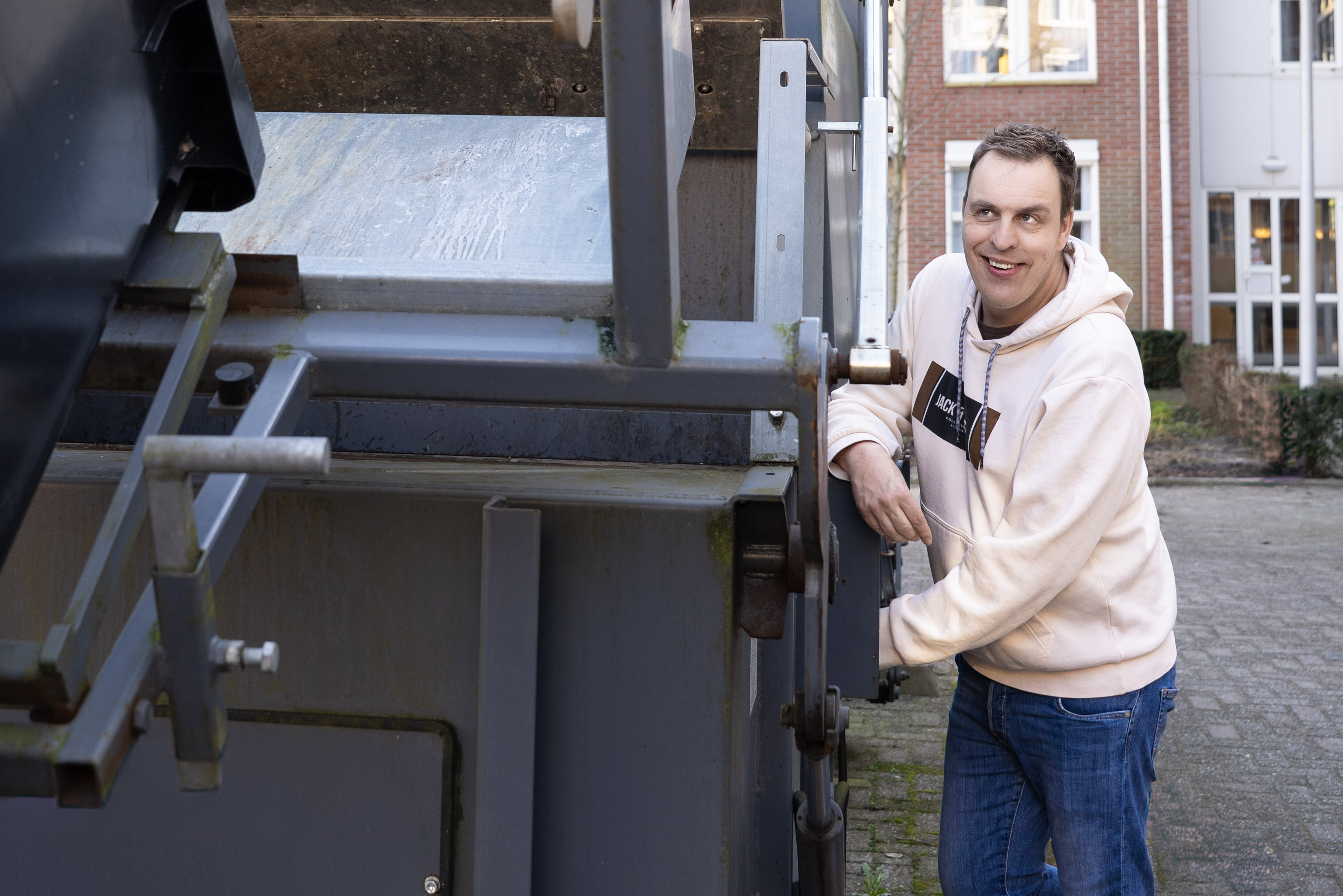 Arjen (man) bij de afvalpers (grote machine)