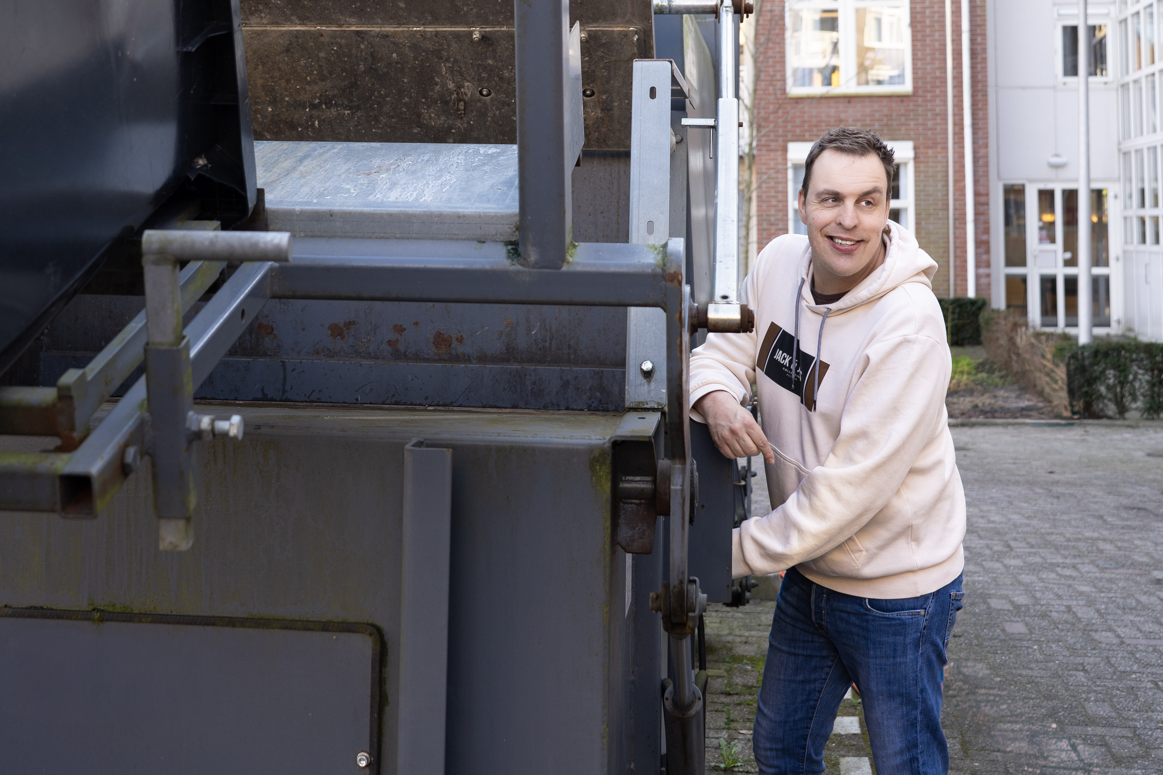 Arjen (man) bij de afvalpers (grote machine)
