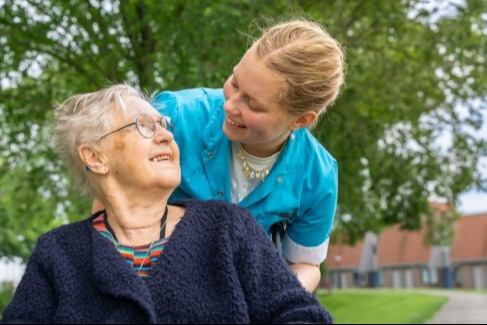 Vrouw in rolstoel en verpleegkundige kijken elkaar aan